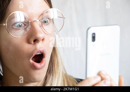 La ragazza guarda il telefono e le meraviglie, l'emozione di gioia e sorpresa dalla chiamata Foto Stock