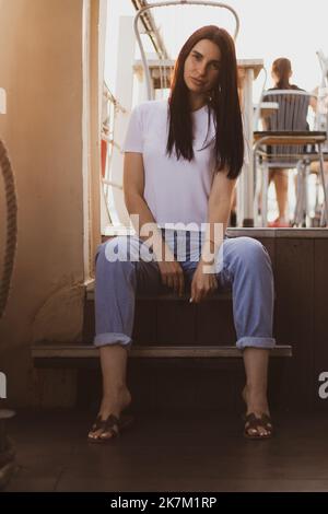 Una ragazza siede su una nave da diporto sul ponte d'estate al sole in Ucraina, una ragazza siede sui gradini Foto Stock