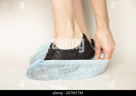 gambe femminili in scarpe nere e stivali usa e getta blu su sfondo bianco, copriscarpe protettive, copriscarpe Foto Stock