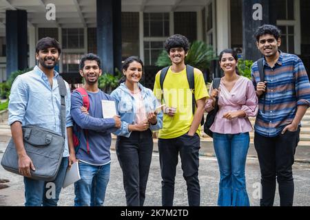 Gruppo di studenti felici in piedi con libri e backback guardando la fotocamera al campus universitario - concetto di amicizia, di convivenza e di istruzione. Foto Stock