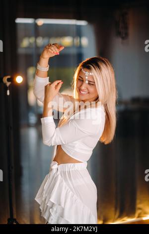 Bella ragazza sorridente in un vestito bianco ballare in palestra Foto Stock