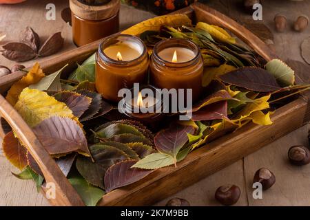 Le candele di soia bruciano in vasi di vetro. Foglie di albero. Comfort a casa. Candela in un vaso marrone. Profumo e luce. Candela profumata fatta a mano. Aromaterapia. Umore autunnale. Arredamento accogliente casa in autunno. Decorazione festiva. Foto Stock