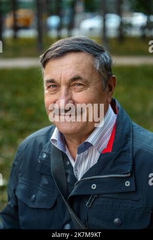 Ritratto di un uomo anziano penitente seduto sulla panchina, nel parco pubblico, all'aperto. Vecchio uomo che si rilassa all'aperto e guarda lontano. Ritratto di anziani m Foto Stock