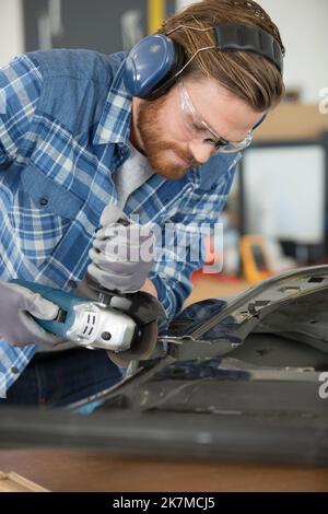 operatore che utilizza una smerigliatrice angolare su una porta dell'auto Foto Stock