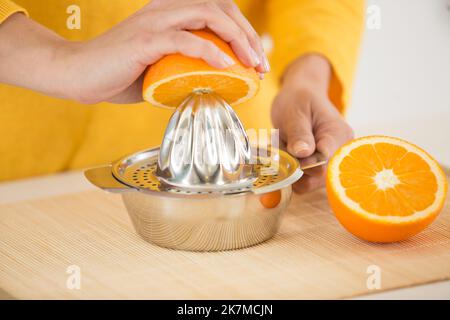 le mani spremono il succo di un'arancia Foto Stock