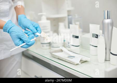 spennellare con crema in mani di estetista Foto Stock