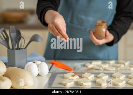 Uno chef in un grembiule blu cosparge la cannella sugli sbozzi di pasta per biscotti in un panificio privato in casa Foto Stock