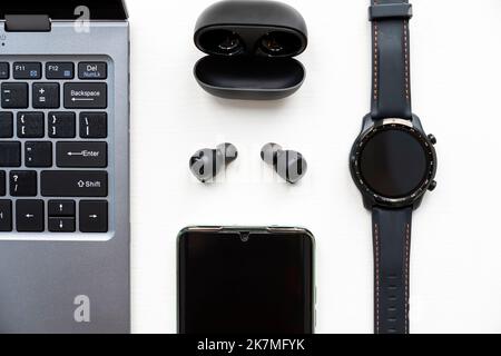 Notebook, smartphone, cuffie wireless e orologio su sfondo bianco. Gadget moderni. Vista dall'alto Foto Stock