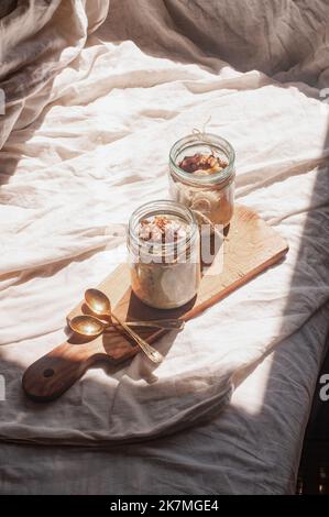 Delizioso durante la notte non cuoco vegan crudo farina d'avena rustica in un vaso con banana e datteri su sfondo minimalistic bello e neutro beige Foto Stock