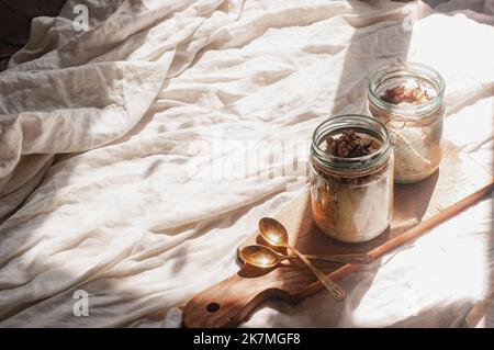 Delizioso durante la notte non cuoco vegan crudo farina d'avena rustica in un vaso con banana e datteri su sfondo minimalistic bello e neutro beige Foto Stock