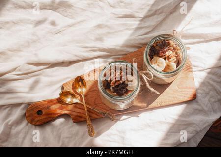 Delizioso durante la notte non cuoco vegan crudo farina d'avena rustica in un vaso con banana e datteri su sfondo minimalistic bello e neutro beige Foto Stock