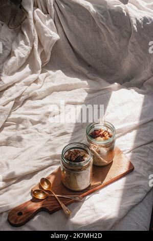 Delizioso durante la notte non cuoco vegan crudo farina d'avena rustica in un vaso con banana e datteri su sfondo minimalistic bello e neutro beige Foto Stock