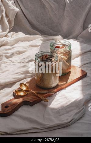 Delizioso durante la notte non cuoco vegan crudo farina d'avena rustica in un vaso con banana e datteri su sfondo minimalistic bello e neutro beige Foto Stock