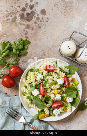Cibo italiano - insalata con pasta senza glutine, spinaci, pomodori, fagioli e formaggio feta su un tavolo di pietra. Cibo sano, antipasto vegetariano. Visualizza da Foto Stock