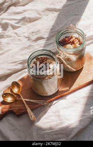 Delizioso durante la notte non cuoco vegan crudo farina d'avena rustica in un vaso con banana e datteri su sfondo minimalistic bello e neutro beige Foto Stock