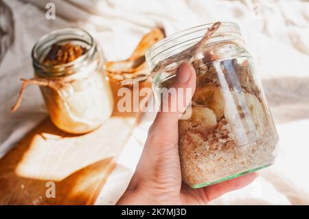 Delizioso durante la notte non cuoco vegan crudo farina d'avena rustica in un vaso con banana e datteri su sfondo minimalistic bello e neutro beige Foto Stock