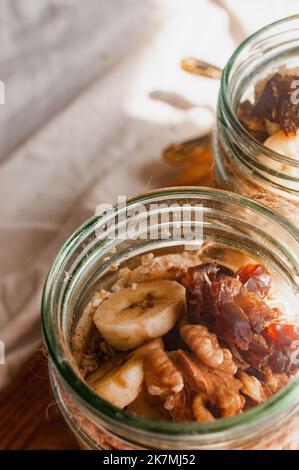 Delizioso durante la notte non cuoco vegan crudo farina d'avena rustica in un vaso con banana e datteri su sfondo minimalistic bello e neutro beige Foto Stock