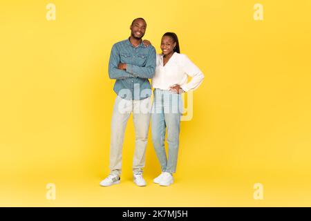 Sposi afro-americani felici che si levano in piedi su sfondo giallo Foto Stock