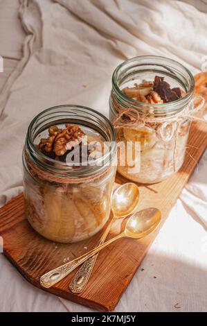 Delizioso durante la notte non cuoco vegan crudo farina d'avena rustica in un vaso con banana e datteri su sfondo minimalistic bello e neutro beige Foto Stock