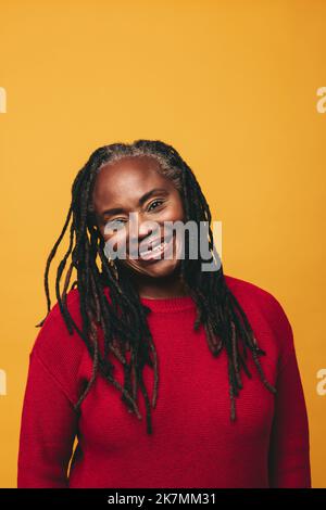 Ritratto di una donna matura con dreadlock sorridente alla fotocamera mentre si trova sullo sfondo di uno studio. Allegra donna nera che abbraccia natura Foto Stock