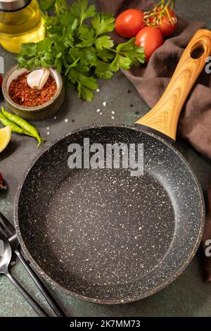 Cucina di fondo con padella. Padella vuota, verdure, spezie ed erbe su sfondo scuro del tavolo. Foto Stock