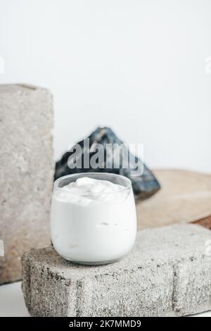 Yogurt o panna acida in vetro su fondo bianco con pietra e rocce. Concetto di base dei prodotti lattiero-caseari. Spazio di copia Foto Stock