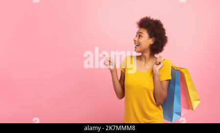 Felice giovane misto razza femmina con capelli ricci con molte borse con acquisti, punta dito a vuoto spazio Foto Stock