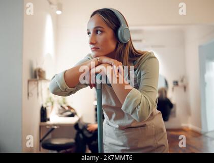 Donna, che pulisce e stanco con la musica in cuffie mentre pulisce la stanza in casa. Più pulito, pensando e contemplando mentre ascolti la radio, podcast Foto Stock