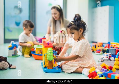 preschoolers costruire con giocattoli e cubi e godere in asilo con l'insegnante, attività creative per i bambini. Foto di alta qualità Foto Stock