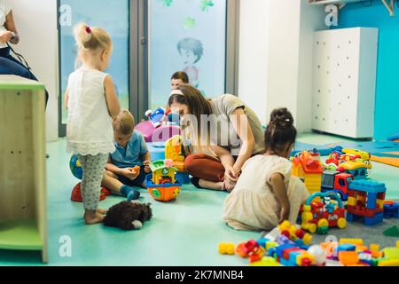 foto completa di una stanza nell'asilo, bambini che giocano con il loro insegnante e costruiscono case, navi e altre cose. Foto di alta qualità Foto Stock