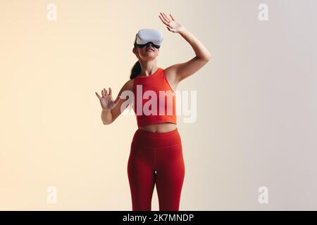 Felice giovane donna che interagisce con il metaverse in uno studio. Giovane donna attiva che guarda intorno mentre indossa una cuffia per la realtà virtuale. Giovane allegro Foto Stock