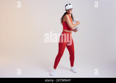 Felice giovane donna sorridente mentre si lavora in realtà virtuale. Giovane donna attiva che gioca un gioco di fitness con controller di gioco. Giovane donna atletica Foto Stock