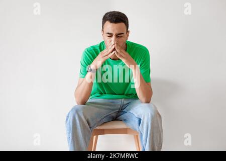Giovane arabo stanco che sbadigliava, ragazzo esausto che copriva la bocca con le mani, sentendosi annoiato e sonnolento, seduto sulla sedia Foto Stock