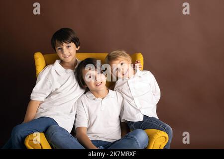 Bambini, fratelli ragazzi in camicie bianche, abbigliamento casual, seduti su una poltrona gialla su uno sfondo isolato, ritratto elegante Foto Stock