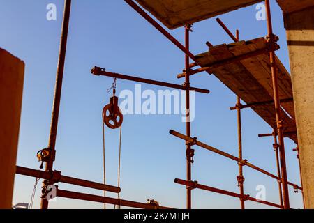 La bobina industriale in ferro arrugginito con la fune attaccata per il ponteggio con i fili è stata installata per sollevare il carico, cielo blu è sullo sfondo. Foto Stock