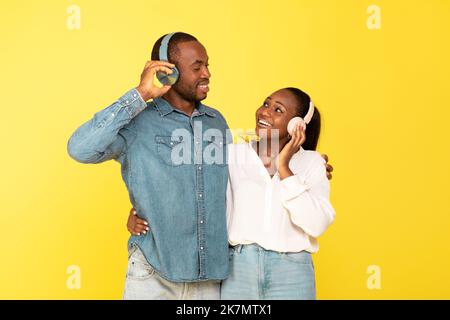 Happy Black Couple ascoltare musica indossando cuffie, sfondo giallo Foto Stock