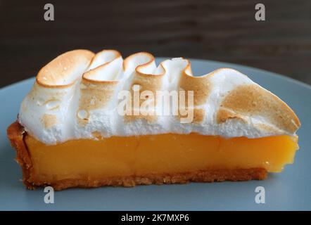 Closeup una fetta di delizioso limone Meringue Tart su un piatto blu Foto Stock