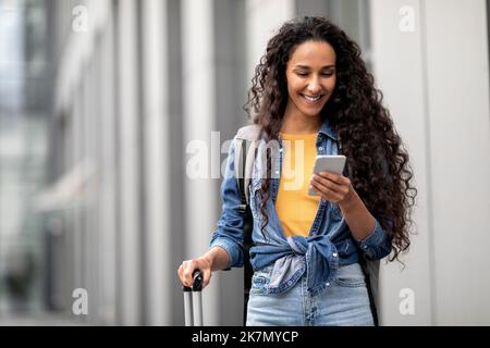 Felice donna mediorientale che viaggia da sola, utilizzando lo smartphone Foto Stock