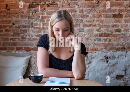 Giovane donna sognante scrivere piani futuri e obiettivi nel proprio diario che riposa in una caffetteria accogliente con tazza di gustoso cappuccino.smiling ragazza hipster facendo ottenere buona idea mentre scrive in blocco note. Foto di alta qualità Foto Stock