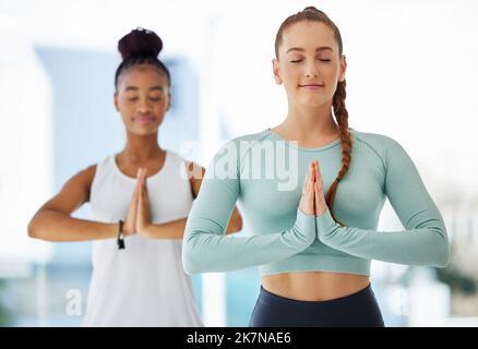 Meditiamo sempre insieme. due giovani donne in piedi insieme e praticare lo yoga in studio. Foto Stock