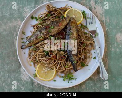In padella sarde fritte con pasta di grano integrale cotta con olio d'oliva, aglio, peperoni e prezzemolo su un piatto Foto Stock