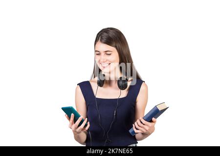 Ragazza contenta studente che tiene un libro e il suo smartphone in mano, isolato su sfondo bianco. Scegliere tra un telefono e un libro di testo, educativo de Foto Stock