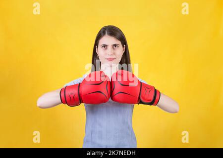 Giovane donna con i guanti di boxe rossi si alza in posizione di combattimento, pugni i pugni. Ritratto di determinata ragazza preparata per la battaglia isolato su Foto Stock