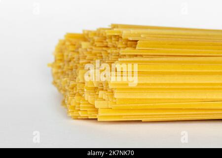 Fettuccine di durum crude su fondo bianco. Spaghetti o tagliatelle crudi. Foto Stock