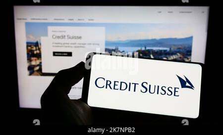 Persona che tiene il cellulare con il logo della società finanziaria Credit Suisse Group AG sullo schermo di fronte alla pagina web aziendale. Messa a fuoco sul display del telefono. Foto Stock