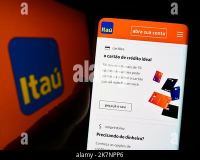 Persona che tiene uno smartphone con il sito web della società brasiliana Itau Unibanco Holding S.A. sullo schermo con il logo. Messa a fuoco al centro del display del telefono. Foto Stock
