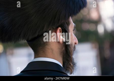 Un uomo ebraico hassidico con un lungo peyus riccio e un cappello di pelliccia di shtreimel che indossa gli airpod di Apple. A Brooklyn, New York City.. Foto Stock