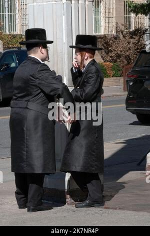 2 i ragazzi hassidici vestiti di nero e con lunghi peyus ricci parlano fuori della sinagoga Satmar a Williamsburg, Brooklyn, New York. Foto Stock