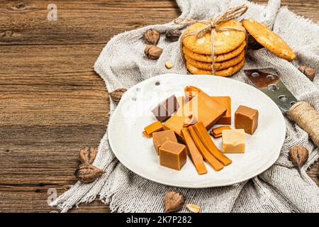 Brunost norvegese con biscotti e noci. Cibo sano e mangiare, ingrediente biologico per la prima colazione. Tradizionale formaggio marrone scandinavo, retro in legno Foto Stock