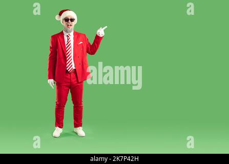 Divertente Babbo Natale a lunghezza intera in un vestito rosso punta con il dito indice in uno spazio vuoto per il testo Foto Stock